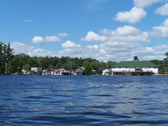 The waterfront of Bala, Ontario, seen across Bala Bay, with boathouses and shops along the shore.