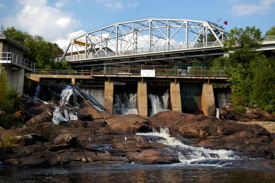 A steel bridge above the dam and rocky falls of the Muskoka River in Bracebridge, Ontario.