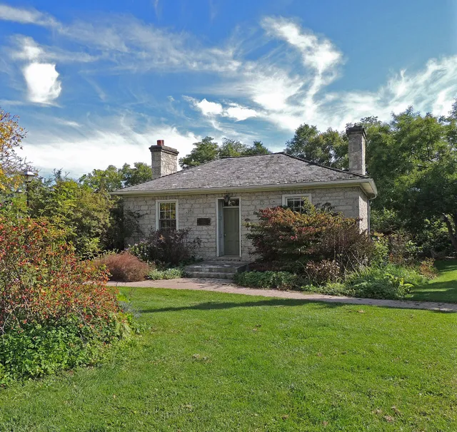 A one-storey stone cottage with a front lawn and gardens in Cambridge, Ontario.