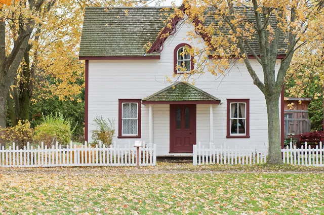 A small white two-storey house with a picket fence and autumn leaves, at Fanshawe Pioneer Village, London, Ontario.