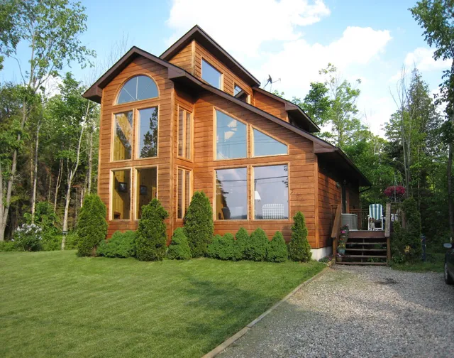 A modern wood-clad house with a front lawn and gravel driveway, in Paudash, Ontario.